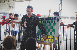 O sargento Nathaniel, vice-campeão de xadrez no Norte, explica as técnicas do esporte aos alunos. O quadro magnético e peças fazem parte do material doado pelo projeto